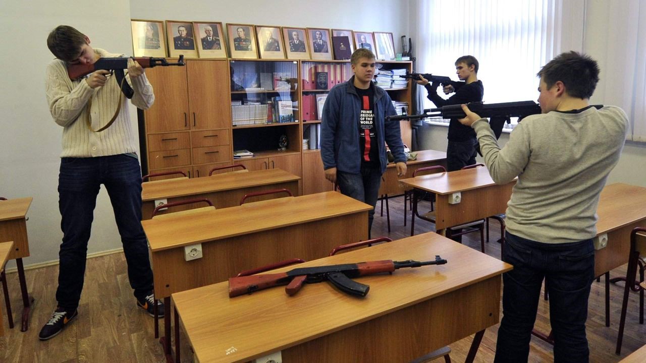 教室で小銃を構えるロシアの高校生。友だちを敵に見立て、銃口を向ける（2023年、ロシア反体制メディアより）