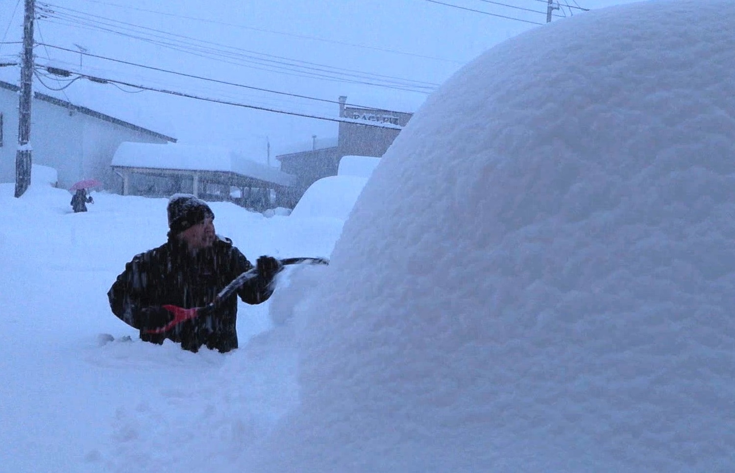 腰まで雪に埋まりながら車の除雪をする市民