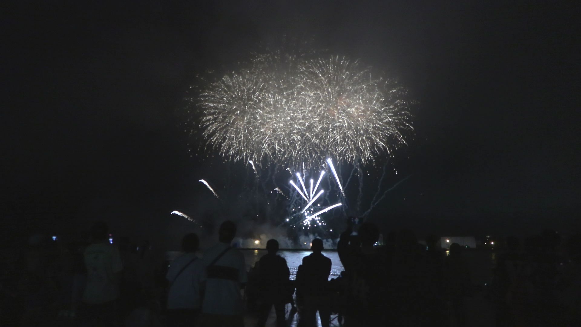 海上に打ちあがる花火を楽しむ観客